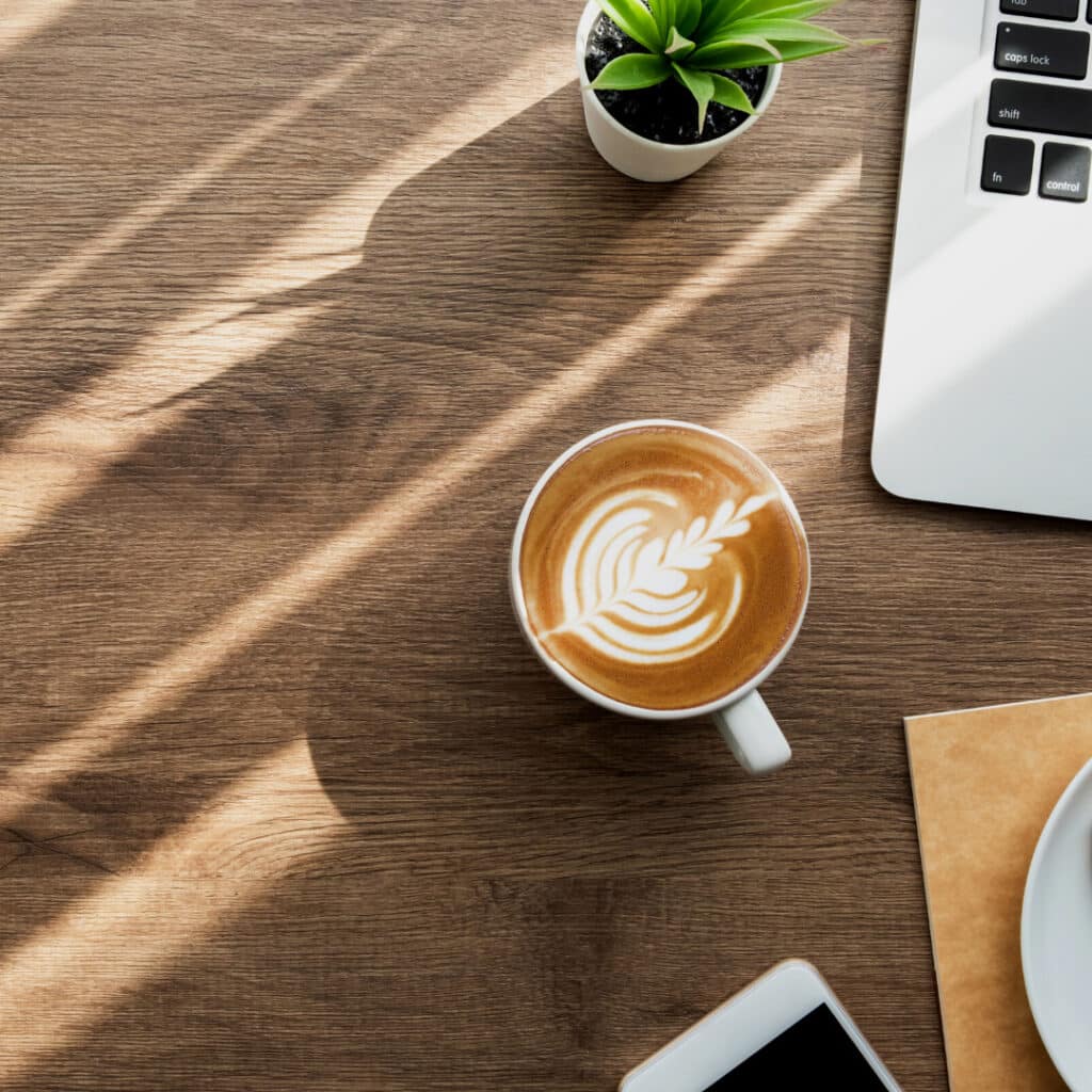 coffee with latte art on desk with laptop, phone and plant in peripheral view